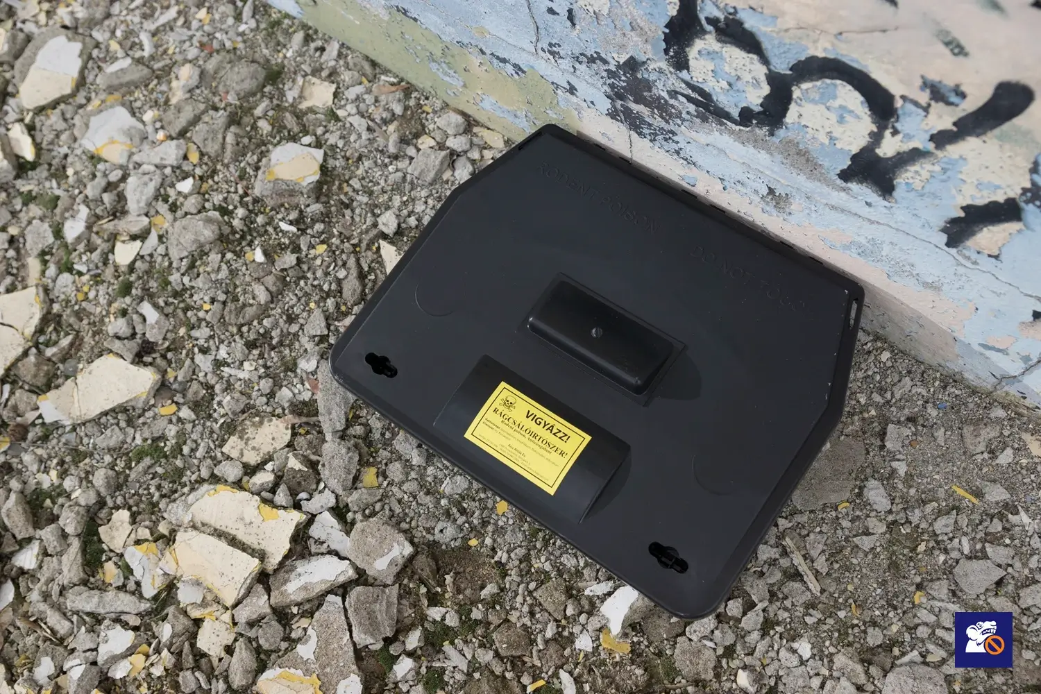 Zárható patkányláda figyelmeztető felirattal épület falánál, kültéri rágcsálóirtás során
